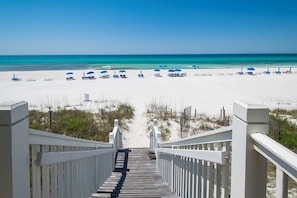 A wooden staircase leading to a beach with white sand and blue umbrellas. - Lakefront dog-friendly condo with water views, pool, hot tub & beach access (Panama City Beach)