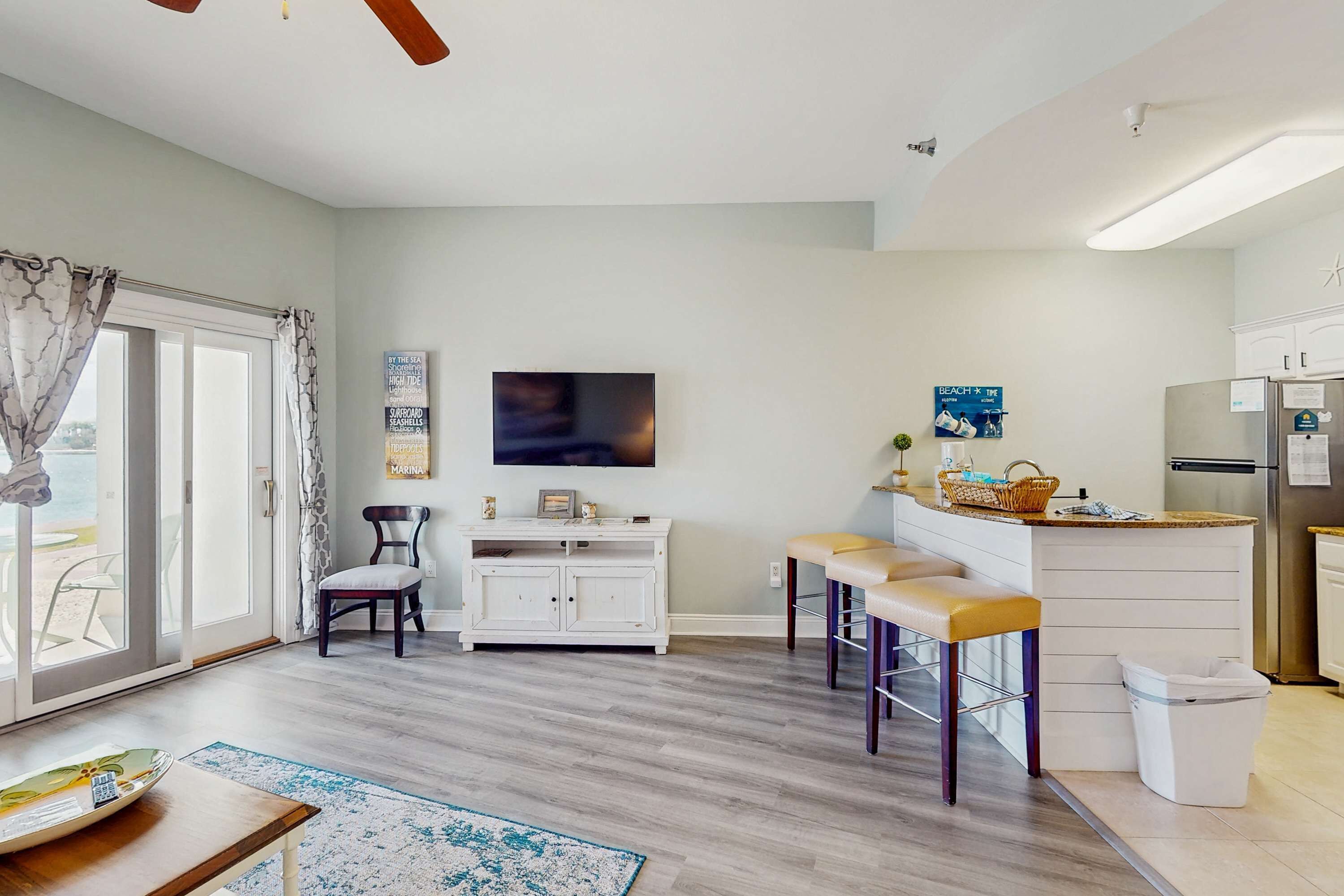Una cocina moderna con una isla central, taburetes de bar, un refrigerador y un televisor en la pared.