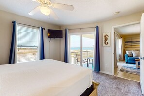 A bedroom with a large bed, a ceiling fan, a TV, and a balcony with a view of the beach. - Bright condo with shared pool, beach access & central location (Navarre Beach)