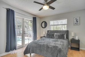 Ein Schlafzimmer mit Bett, Deckenventilator, Nachttisch, Fenster mit Jalousien und Blick auf einen Pool.