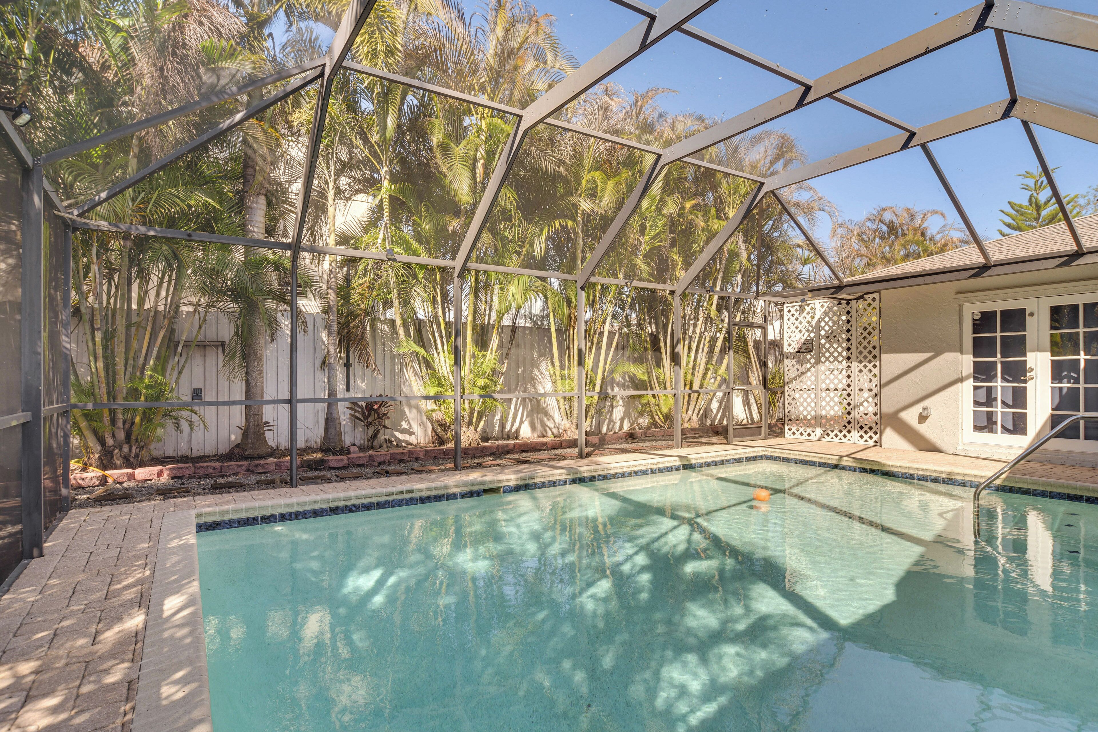 A swimming pool with a glass enclosure, surrounded by palm trees and a white fence.