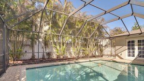 Une piscine entourée d’une paroi de verre, bordée de palmiers et d’une clôture blanche.