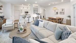 Een moderne woonkamer met een bank, fauteuils, een salontafel en een eetgedeelte met een tafel en stoelen.