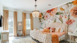 A bedroom with a tufted bed, a chandelier, a fluffy rug, and a floral wallpaper. - 3 Mi to Ocean! Family-friendly 30A Getaway w/ Pool (Santa Rosa Beach)