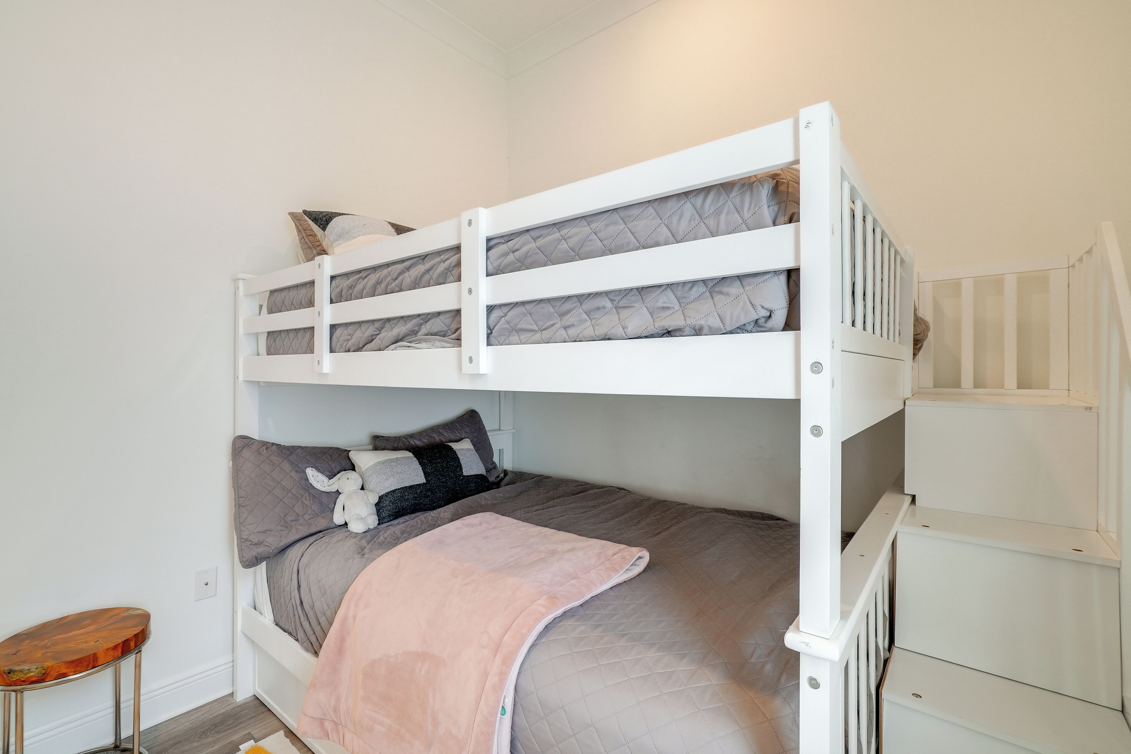 A bunk bed with a wooden ladder, a small wooden stool, and a white wall.