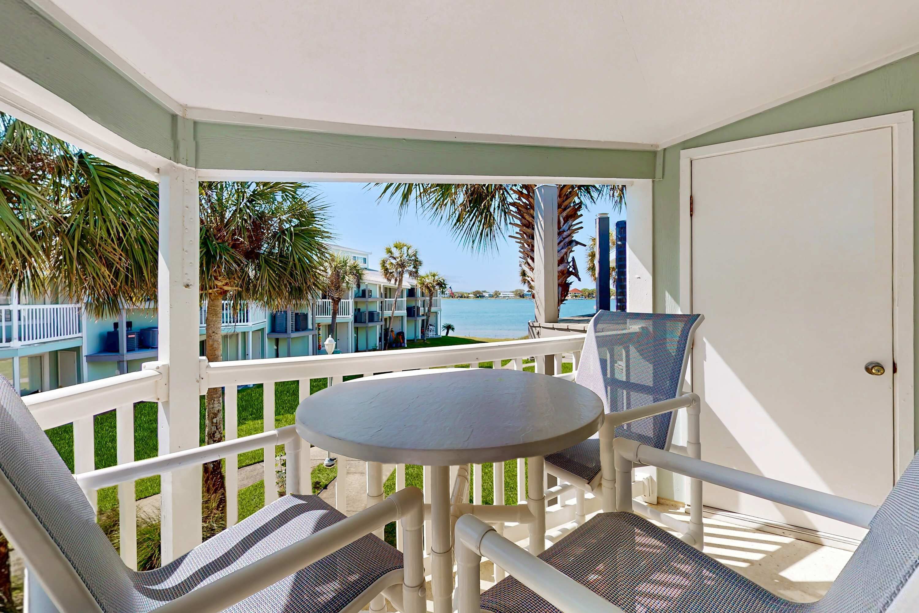 A covered outdoor seating area with a table and chairs, overlooking a pool and buildings.