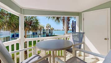 A covered outdoor seating area with a table and chairs, overlooking a pool and buildings.