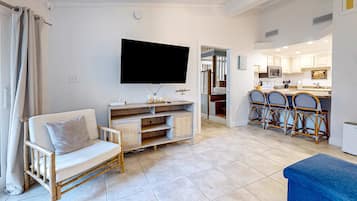 A living room with a sofa, TV, and a kitchen in the background.