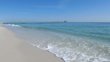 A beach with clear water and a pier extending into the sea.