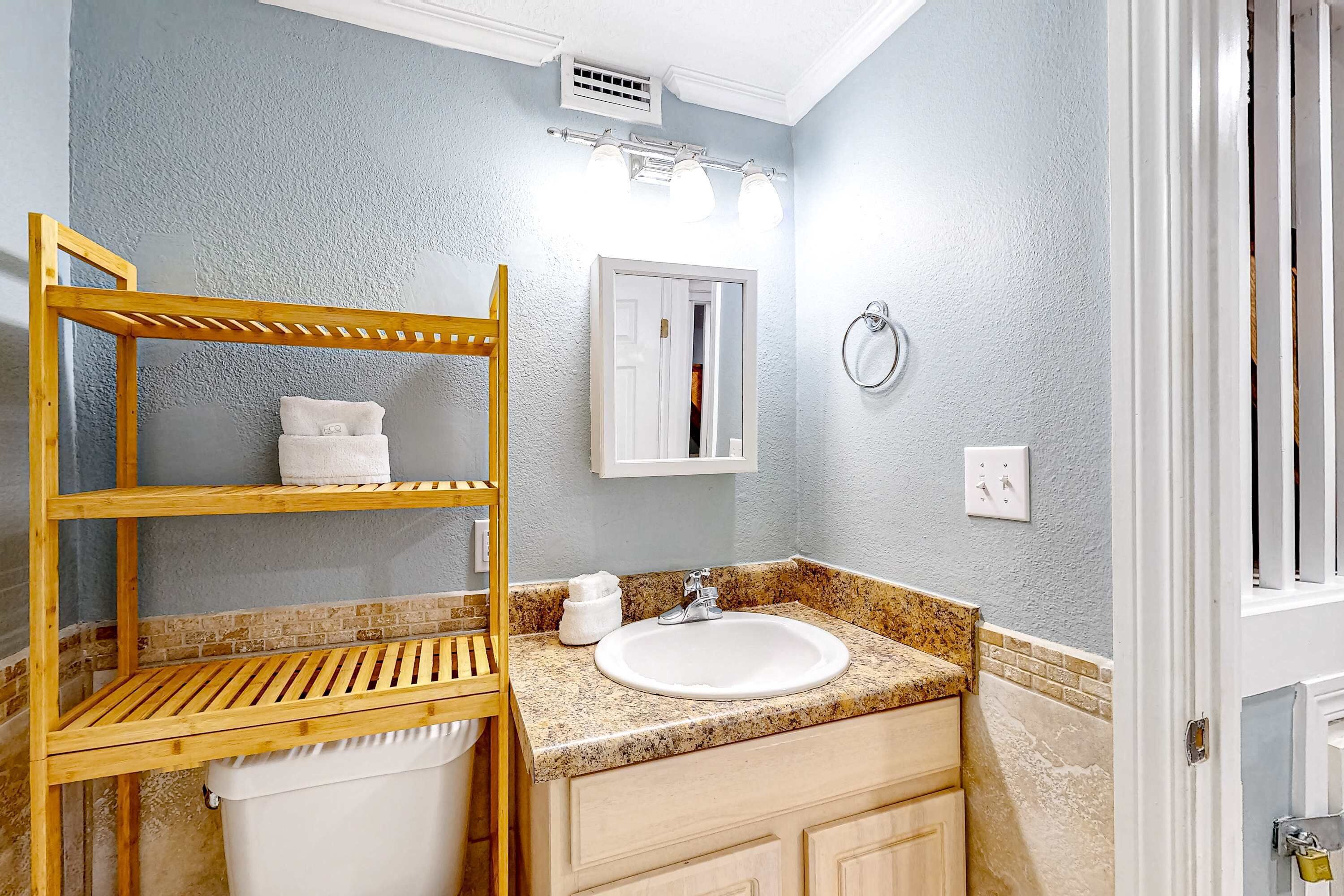 A bathroom with a wooden shelf, a sink, a mirror, and a towel rack.