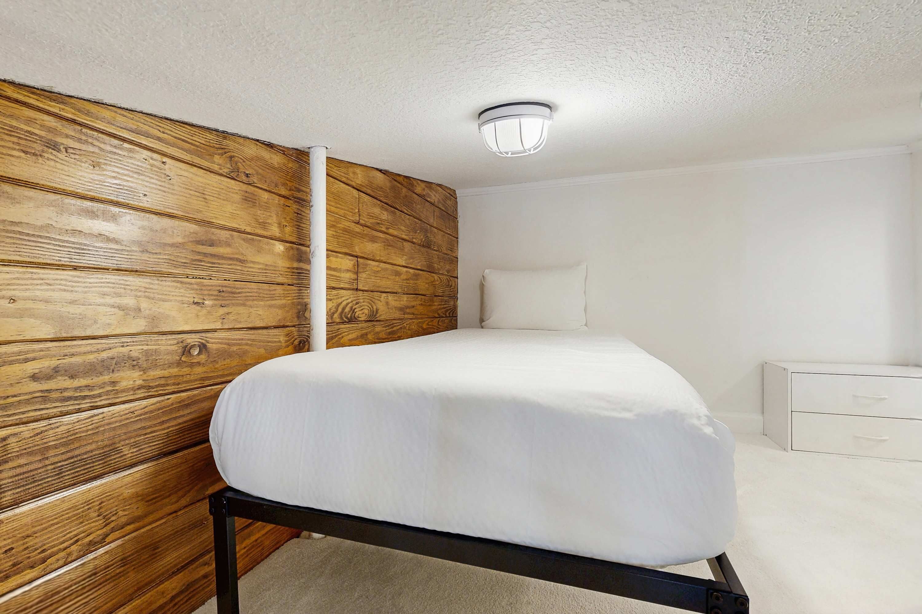 A bedroom with a wooden headboard, a bed with white bedding, a nightstand, and a white dresser.