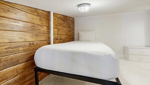 Een slaapkamer met een houten hoofdeinde, een bed met witte beddengoed, een nachtkastje en een witte dressoir.