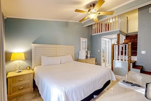 Ein Schlafzimmer mit Bett, Nachttischen, einer Lampe, einem Deckenventilator, einer Treppe und einer Tür.
