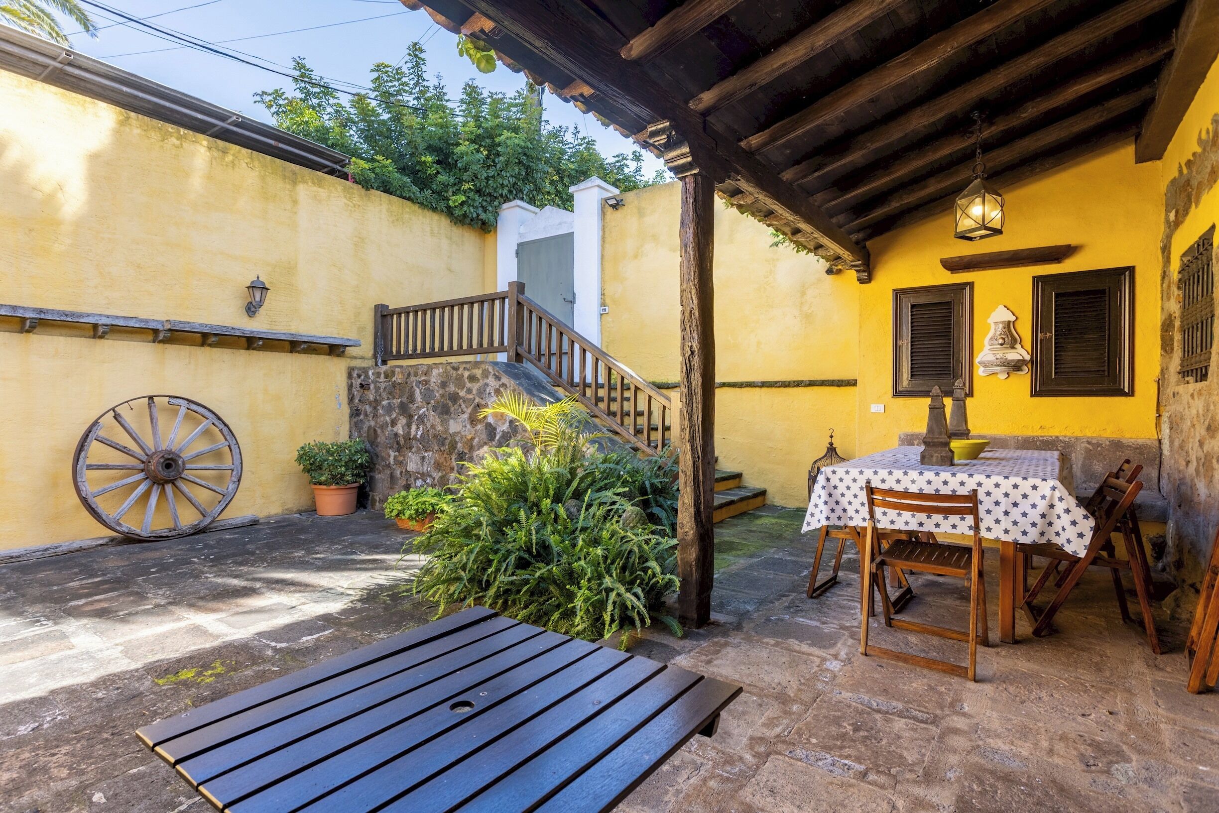 Une terrasse avec une table et des chaises en bois, un escalier en pierre et un mur jaune avec une porte en bois.