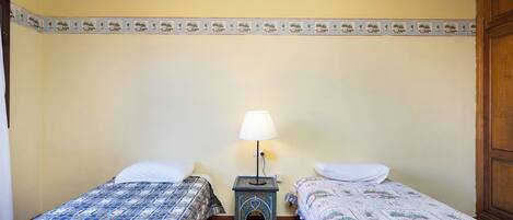 A room with two beds, a small table with a lamp, and a decorative border on the wall.