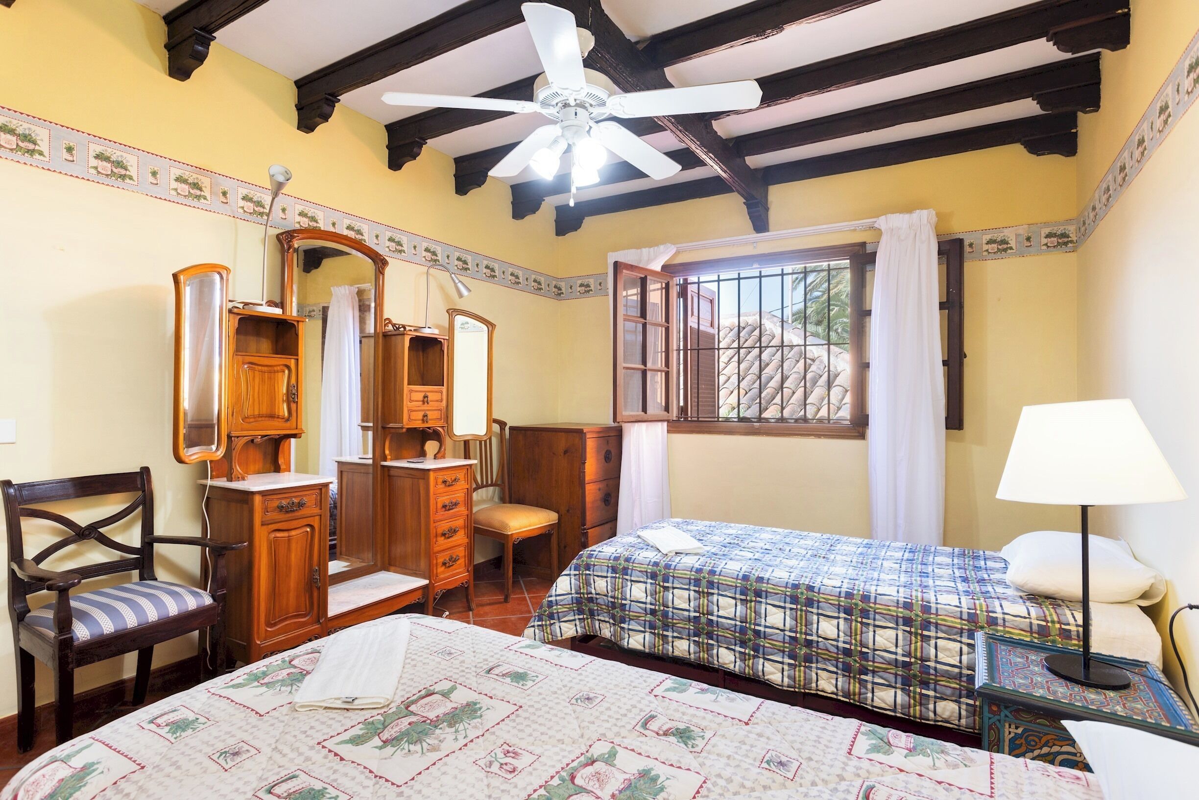 A bedroom with two beds, a wooden dresser, a chair, a mirror, and a window with curtains.
