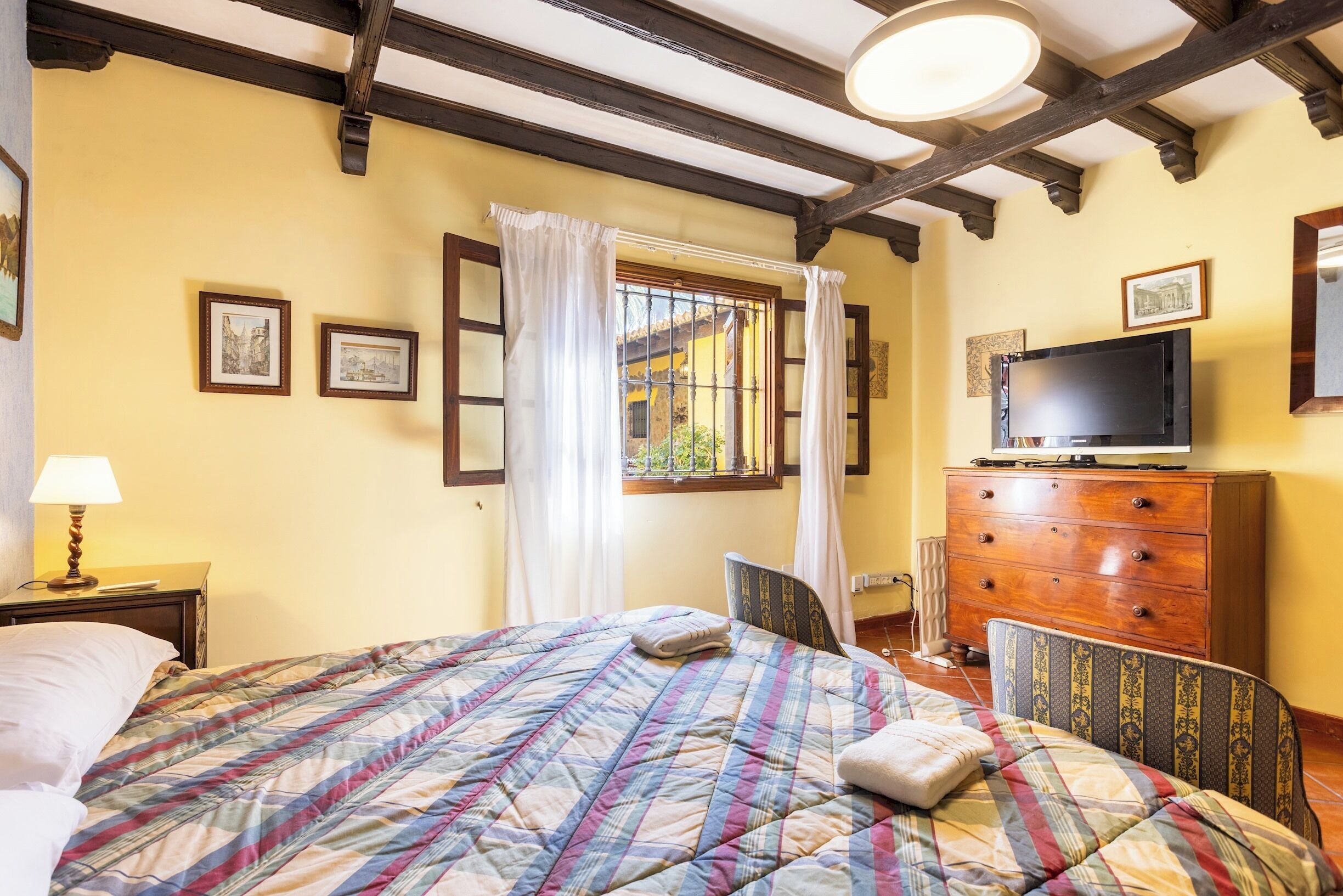 A bedroom with a bed, a dresser, a television, and a window with curtains.