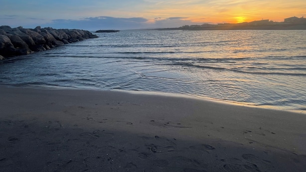 Een strand met een rotsachtige kustlijn en een ondergaande zon.