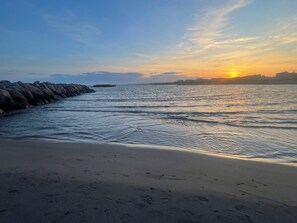 Ein Strand mit felsiger Küste und einem Sonnenuntergang im Hintergrund.