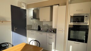 Een compacte keuken met een magnetron, oven en een spoelbak. Er is een houten tafel met stoelen.