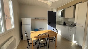Een kleine keuken met een eethoek, witte apparaten en een plafondventilator.