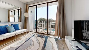 Un salon moderne avec un canapé, un téléviseur et un balcon aménagé avec du mobilier d’extérieur.