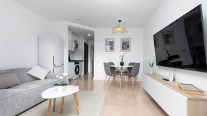 Ein modernes Wohnzimmer mit grauem Sofa, einem kleinen weißen Tisch und einem Essbereich mit grauen Stühlen.
