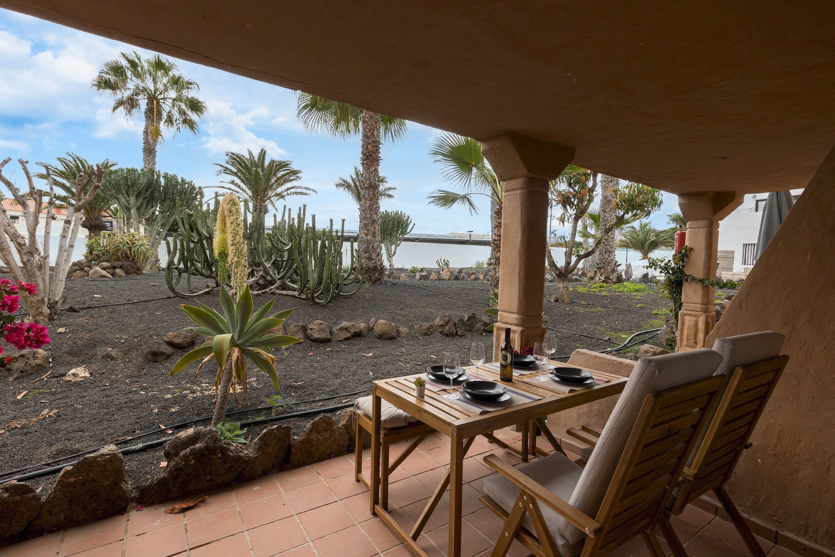 Une terrasse avec une table dressée pour deux personnes, entourée de cactus et de palmiers.
