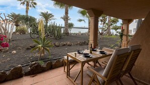 Eine Terrasse mit Tisch für zwei Personen, umgeben von Kakteen und Palmen.