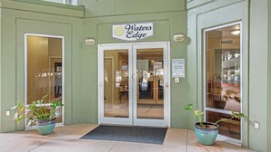 The exterior of Waters Edge, featuring a green facade, double glass doors, and two potted plants. - Stunning top-floor condo with balcony, pool, & beach access - great location (Fort Walton Beach)