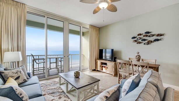 A living room with a large window, a ceiling fan, a television, and a dining area with a table and chairs. - Stunning top-floor condo with balcony, pool, & beach access - great location (Fort Walton Beach)