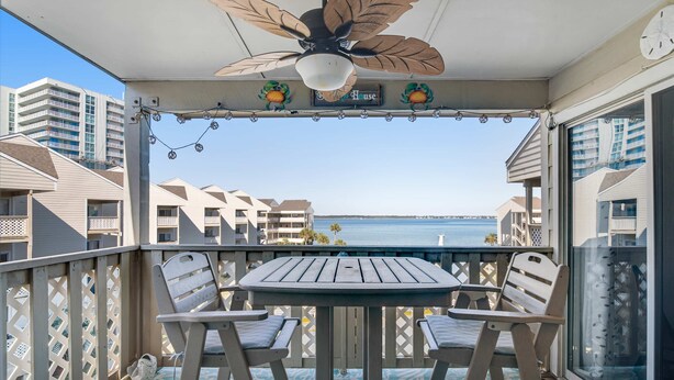 Un balcon avec une table et des chaises, un ventilateur de plafond et une vue sur l’océan et les bâtiments.