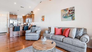 Un salon moderne avec un canapé gris, une table basse et un coin cuisine à l’arrière-plan.
