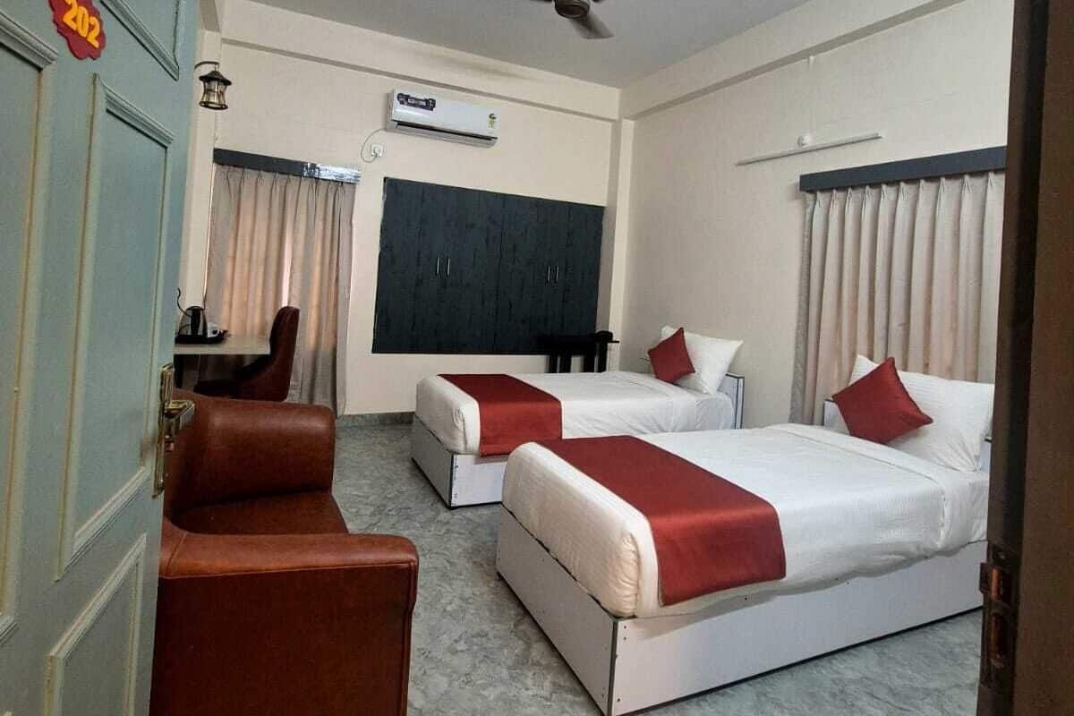 A hotel room with two beds, a desk, a chair, a ceiling fan, and an air conditioning unit.
