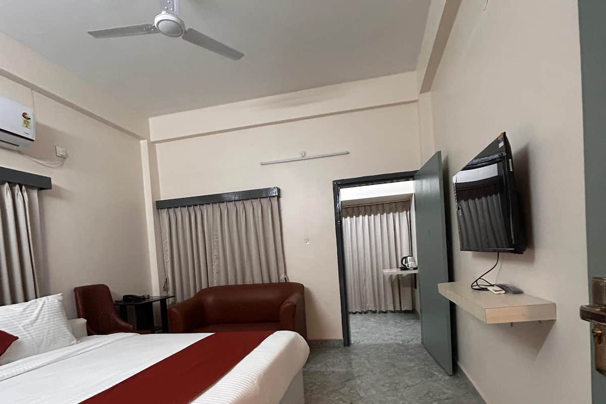 A hotel room with a bed, a desk, a chair, a TV mounted on the wall, and a ceiling fan.
