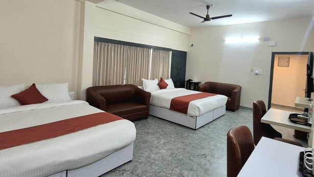 A hotel room with two beds, a sofa, a dining table, and two ceiling fans. - NK GUEST HOUSE (Guwahati)