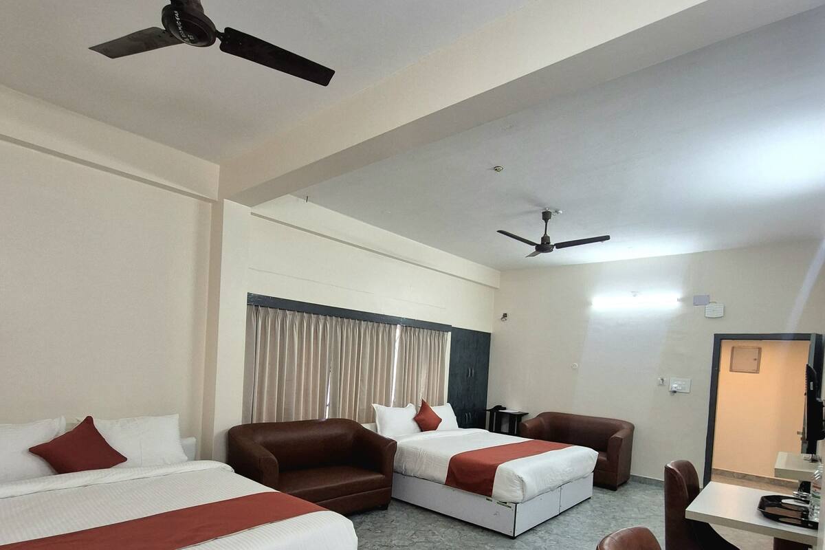 A hotel room with two beds, a sofa, a dining table, and two ceiling fans.