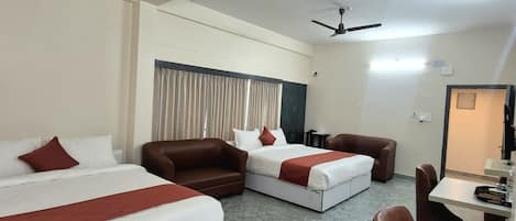 A hotel room with two beds, a sofa, a dining table, and two ceiling fans.