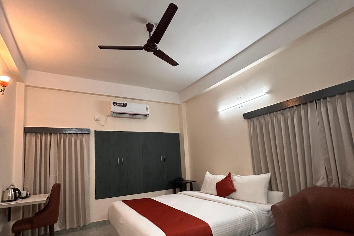 A hotel room with a bed, a desk, a chair, a ceiling fan, and an air conditioning unit.