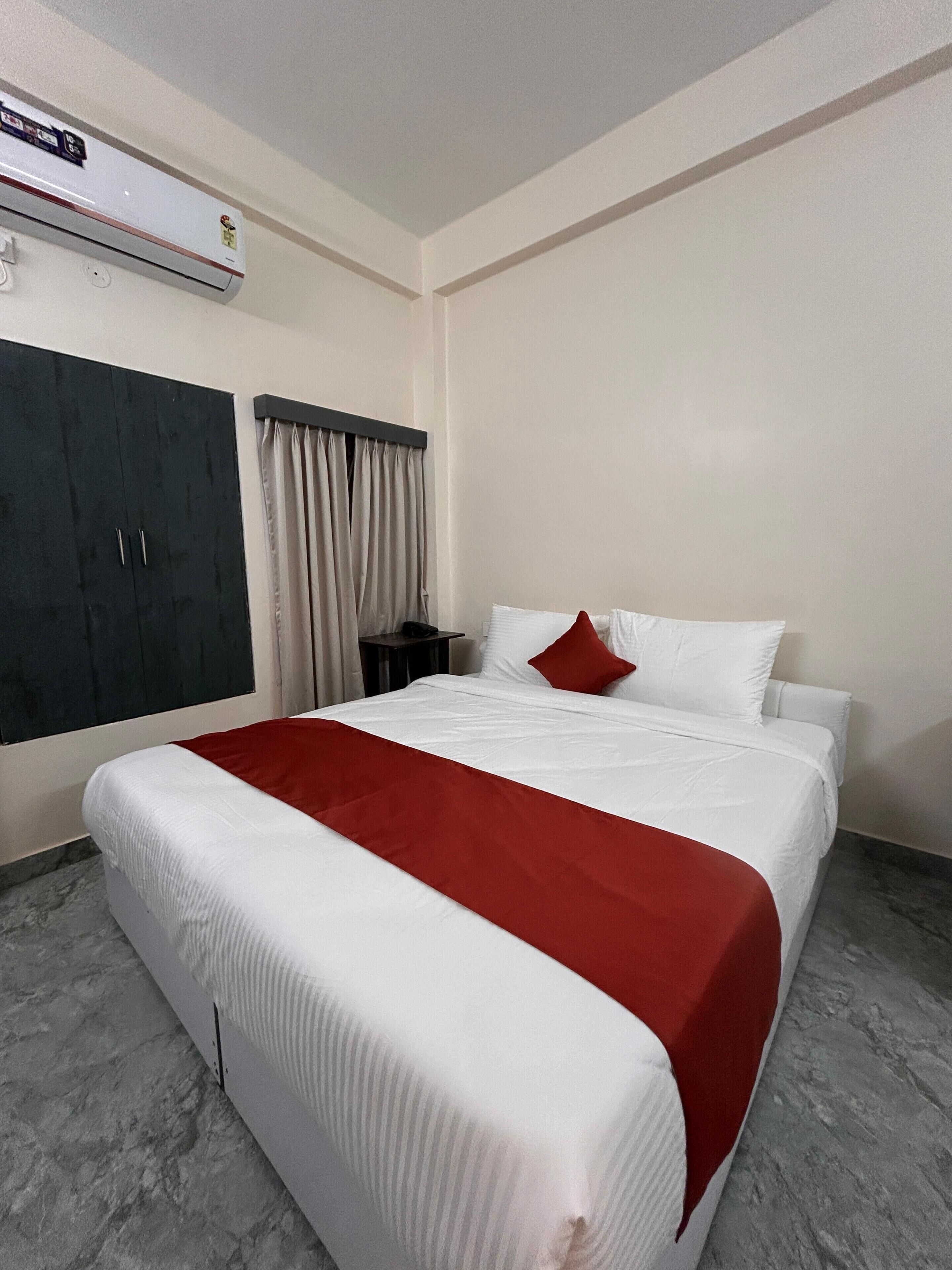 A hotel room with a bed, a wardrobe, a nightstand, and an air conditioning unit.