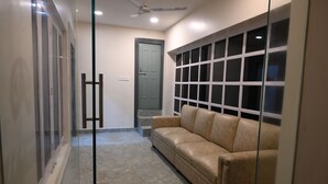 A hallway with a glass door, a beige leather sofa, and a large window with multiple panes. - NK GUEST HOUSE (Guwahati)