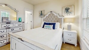 A bedroom with a white bed, a nightstand with a lamp, a dresser, and artwork on the walls. - Beautiful home in a gated community with porches & shared pool,hot tub (Port St. Joe)