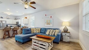 A living room with a blue sofa, wooden coffee table, and a ceiling fan. - Beautiful home in a gated community with porches & shared pool,hot tub (Port St. Joe)