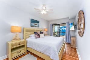 Une chambre à coucher comprenant un lit, deux tables de chevet, un ventilateur de plafond, un tableau, un téléviseur et une vue sur l’extérieur.