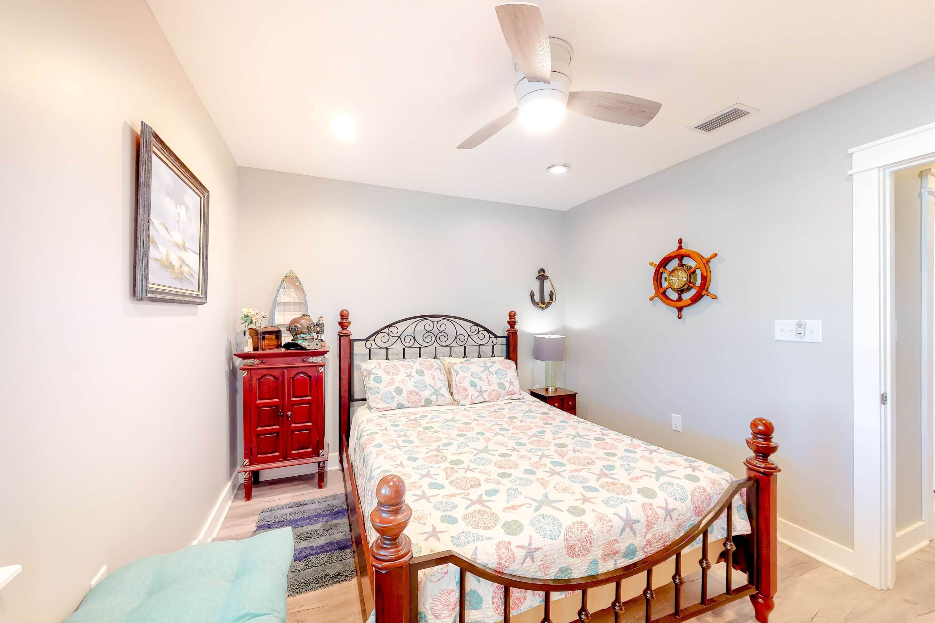 A bedroom with a bed, a ceiling fan, a red dresser, a wall clock, and a door.
