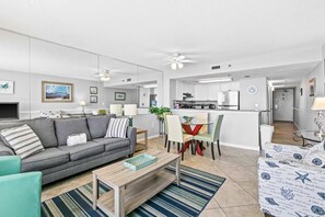 A modern living room with a sofa, coffee table, and chairs, a dining area with a table and chairs, and a kitchen in the background. - Beach-chic 18th floor condo w gulf-front views Indoor & outdoor pool on-site (Destin)