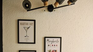 A wall with framed pictures of drinks and a shelf with a coffee maker, a candle, and a box. - Apartment in Aubenas town center, cozy style, office, internet, netflix (Aubenas)