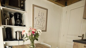 A kitchen with a wooden table, chairs, a vase with flowers, and kitchen appliances. - Apartment in Aubenas town center, cozy style, office, internet, netflix (Aubenas)
