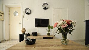 A dining area with a wooden table, a vase with flowers, a black bowl, a remote control, and a flat-screen TV mounted on the wall. - Apartment in Aubenas town center, cozy style, office, internet, netflix (Aubenas)