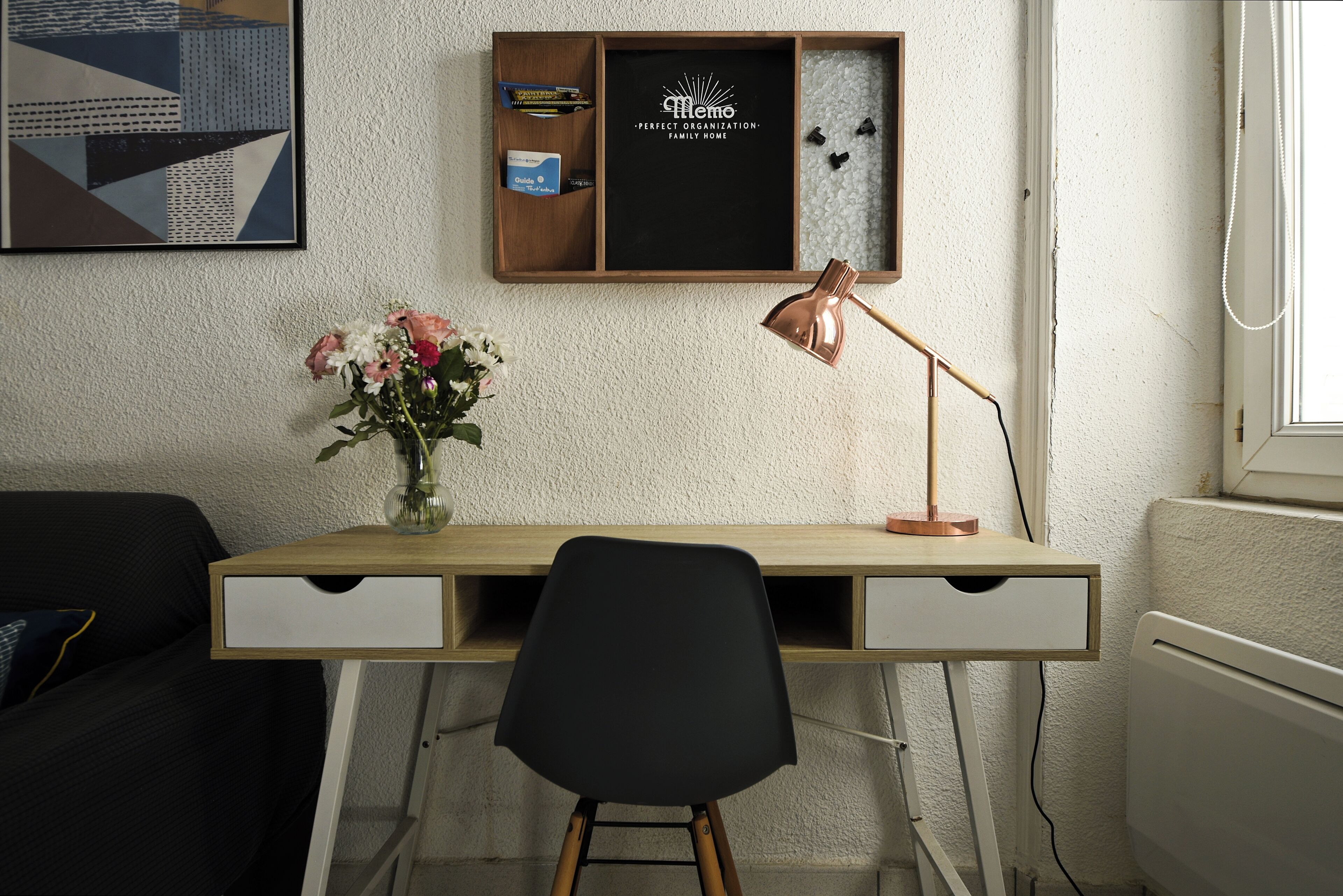 Ein moderner Schreibtisch mit schwarzem Stuhl, einer Schreibtischlampe und einer Vase mit Blumen.